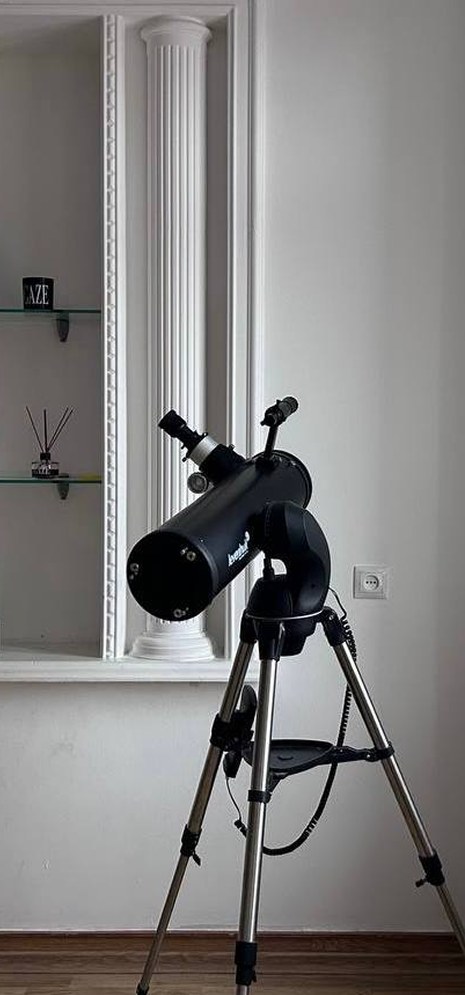 A telescope on a tripod by a window